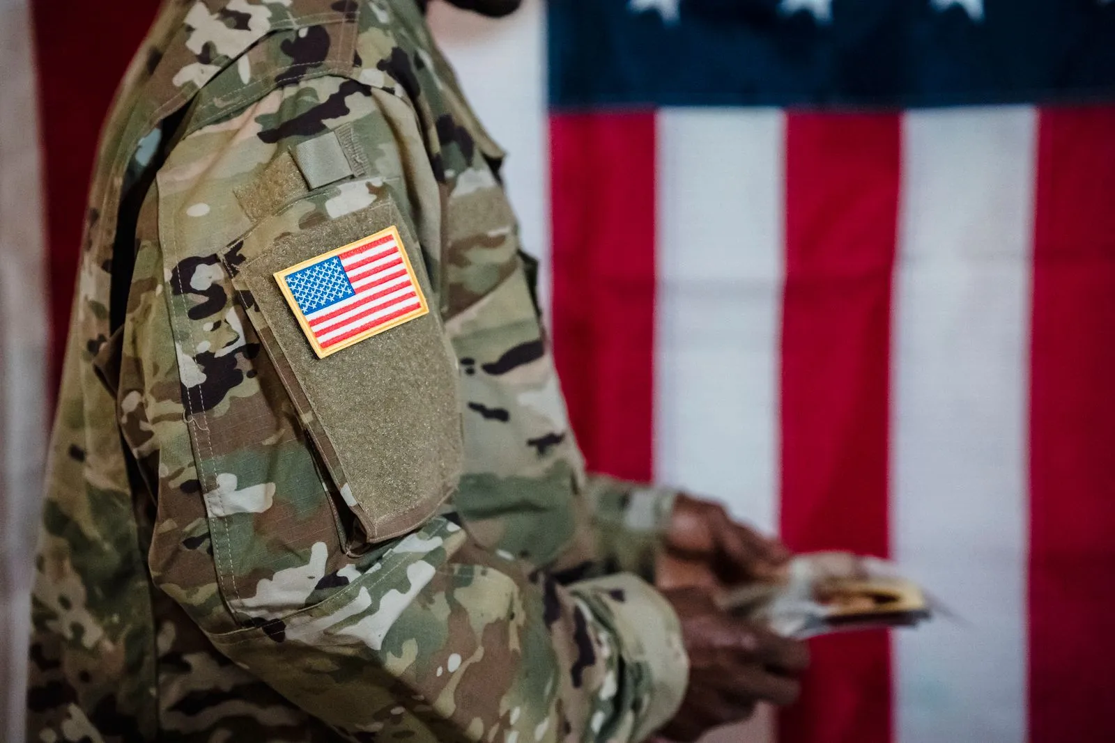 American flag patch on the sleeve of a soldier's uniform, with the flag behind